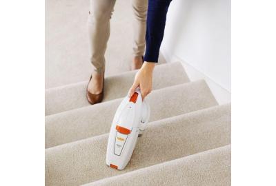 A woman using a handheld vacuum cleaner on a staircase