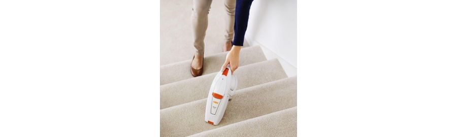 A woman using a handheld vacuum cleaner on a staircase