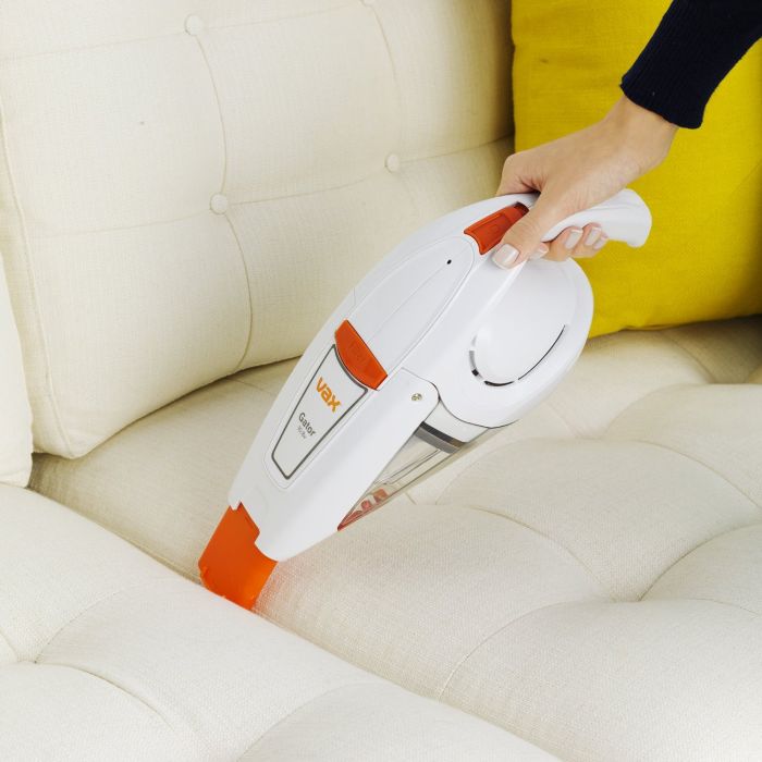 A person cleaning a sofa with a VAX Gater cordless handheld vacuum cleaner